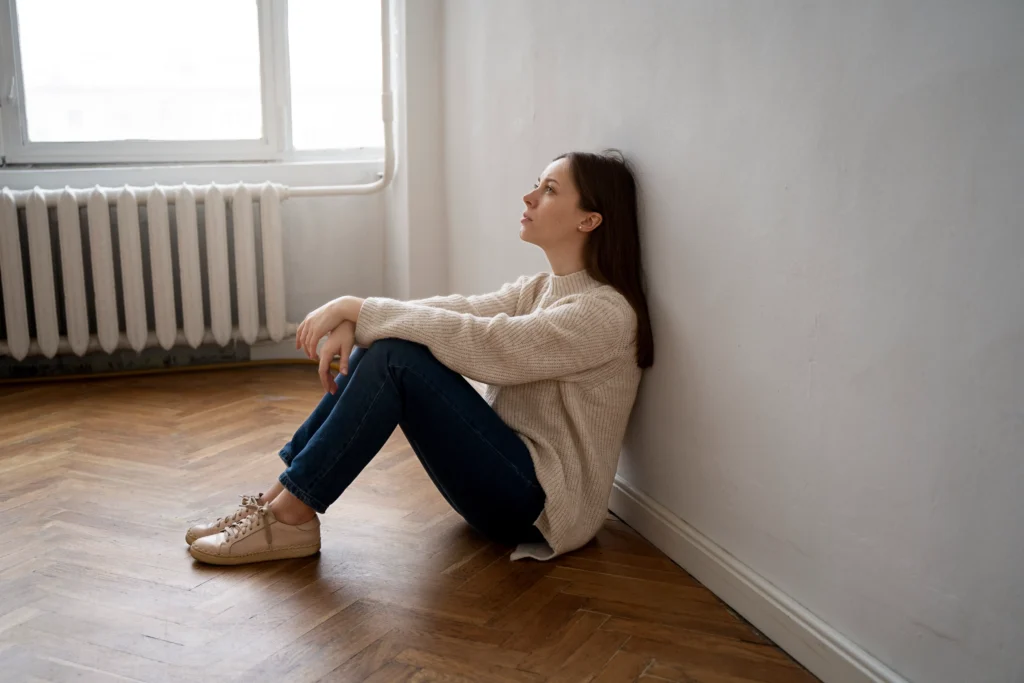 Young woman sitting alone on the floor, leaning against a wall, looking distressed and deep in thought — symbolizing emotional reflection and the need for a trauma test.